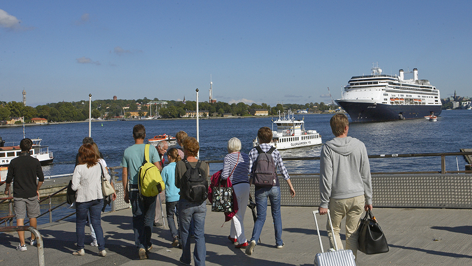 Passagerare på kaj i centrala Stockholm framför stort kryssningsfartyg.