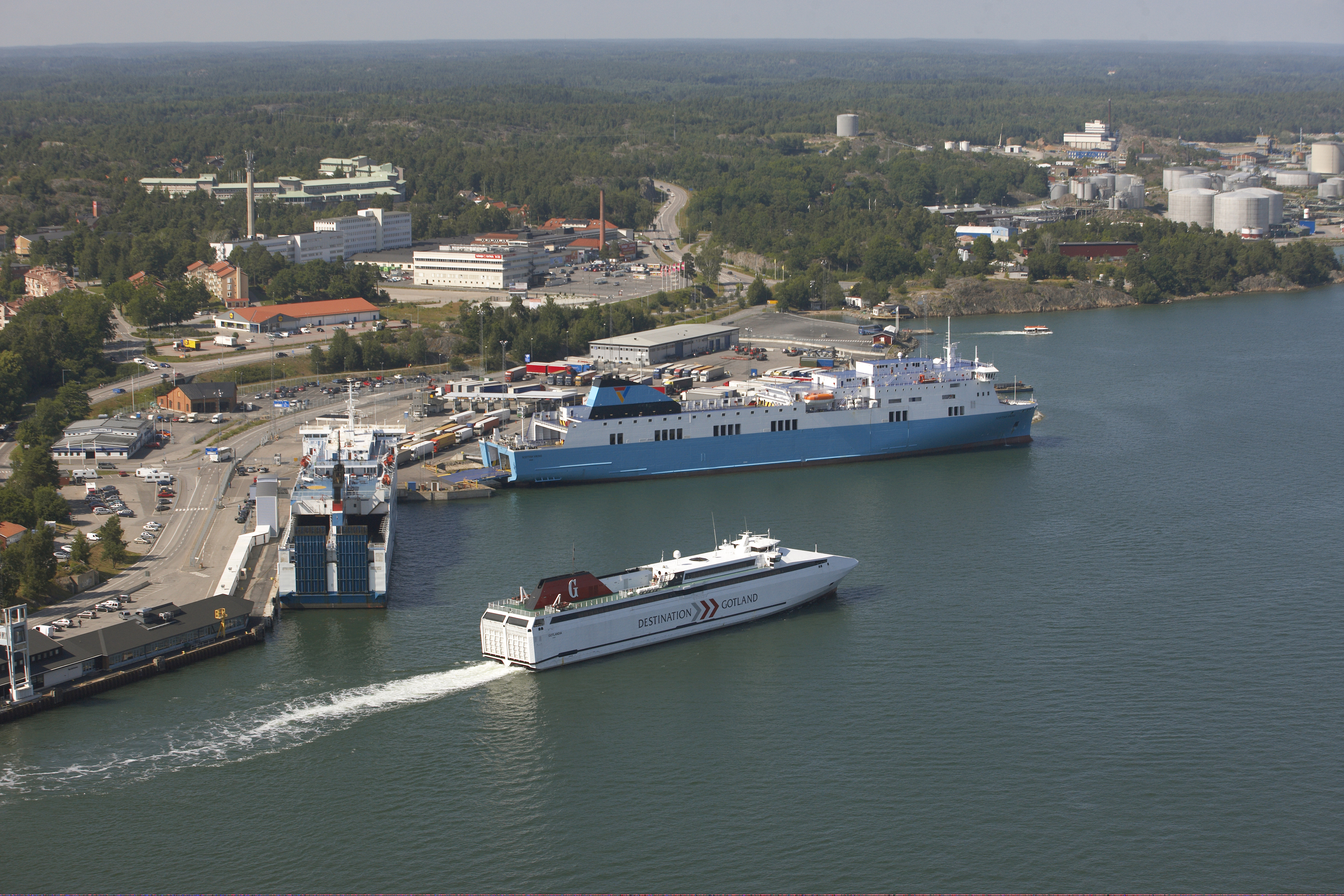 Flygbild över Nynäshamns hamn. Två färjor ligger vid kaj, och en är på väg ut.