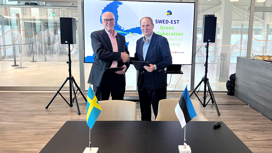 Representanter för Stockholms Hamnar och Tallinns Hamn skakar hand framför en svensk och en estländsk flagga.