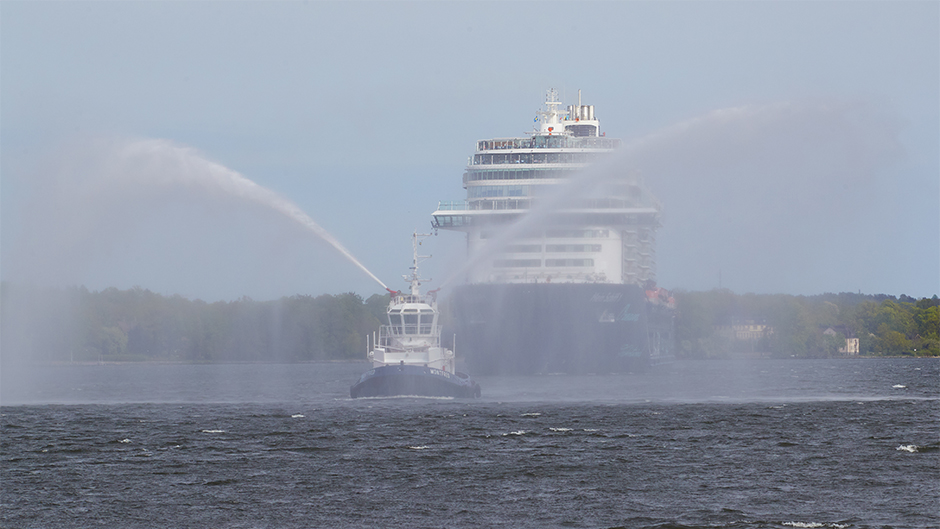 Tugboat shooting water in front of cruise vessel arriving at Port of Stockholm